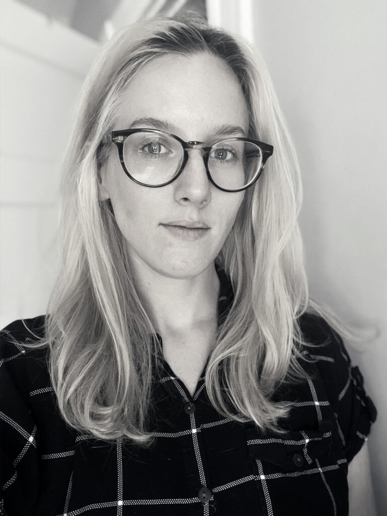 A black and white photo of Alexandra Gallant, a white woman with blonde hair and glasses and a plaid shirt
